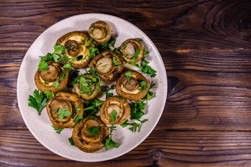 Plate with baked champignons, dill and parsley on a wooden table. Top view