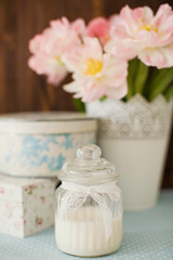 Fototapeta na wymiar White natural candle in vintage glass jar with lace ribbon. Gift boxes with flower ornament. Bouquet of tulips with pink and white petals in white metal vase.