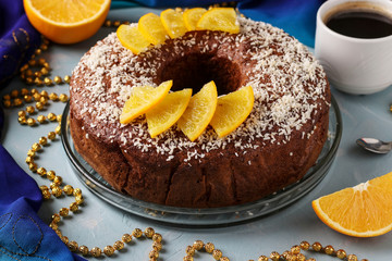 Homemade muffin with oranges with a hole in the center, sprinkled with coconut flakes on a light blue background and a cup of coffee