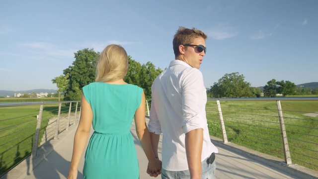 SLOW MOTION, CLOSE UP: Funny shot of a young man looking back at another beautiful woman during a date with his girlfriend. Guy holding his girlfriend's hand turns around to check out a pretty woman.