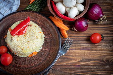 Rice with vegetables. Vegetarian dish. Mushrooms and carrots, onions, spices, hot chili peppers and garlic. Black pepper and zira. Cooking in olive oil. Healthy diet. On a wooden background.