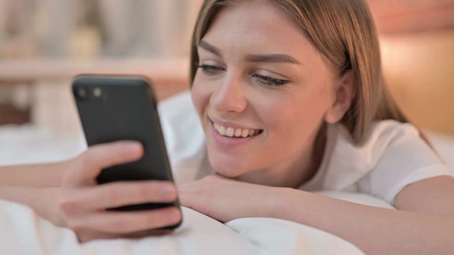 Close up of Happy Young Woman using Smartphone in Bed 