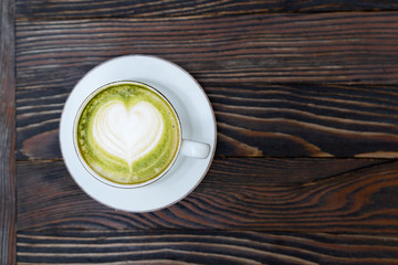 Green matcha tea latte in a white cup on brown wooden background isolated.