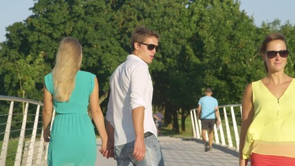 SLOW MOTION, CLOSE UP: Young Caucasian man holding hands with his girlfriend looks back at woman walking by. Jealous blonde girl strikes her boyfriend for looking at another woman walking past them.
