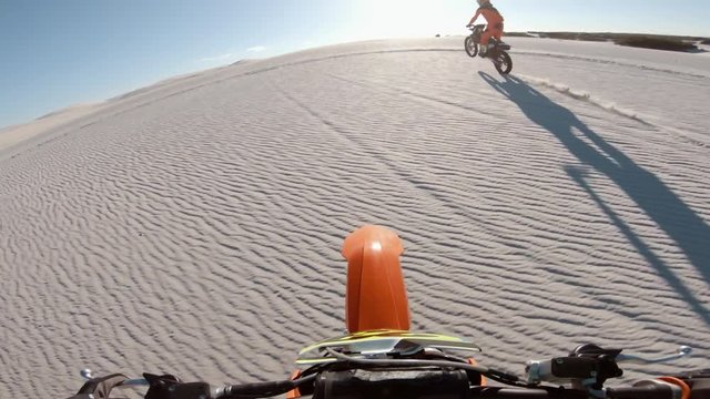Motocross racers racing over sand dunes. Dirt bikers riding motorcycles together. Point of view of a dirt bike rider.