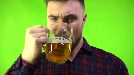 Drunk man in a plaid shirt drinks beer on a green background. Oktoberfest and vacation concept. Funny bearded drunk hipster holds craft beer. Chroma key.