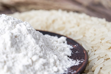 Rice flour in a bowl near the heap of white rice on old boards. Jasmine rice for cooking.