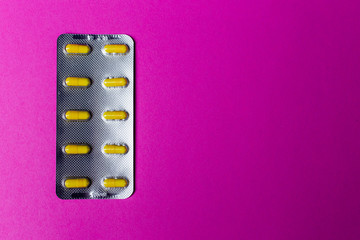 Silver pack of yellow capsules on pink background with copy space