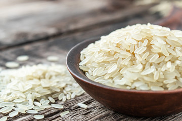 A bowl of white rice against the background of old boards near sprinkled rice. Jasmine rice for cooking.