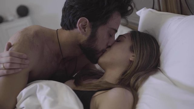 Man kisses his girlfriend goodbye in bed before leaving