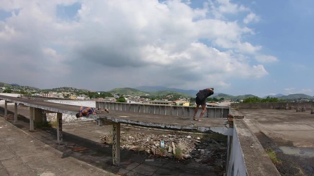 two freerunners perform sideflips and jump from a roof to escape to a window