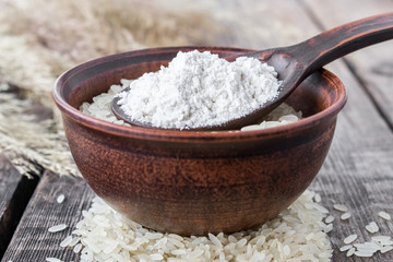 White rice in a bowl with a spoon of white flour on a background of old boards. Jasmine rice for cooking.