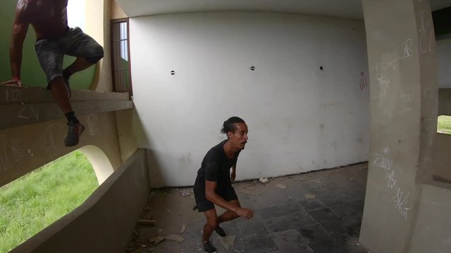 two freerunners climbing down in a park hpuse from the upper floor to perform some jumps