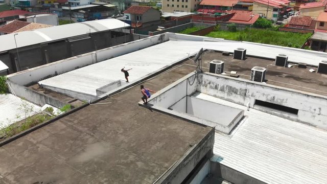 two young freeruners jumping and performing  flips and tricks over obstacles on a rooftop followed bya drone