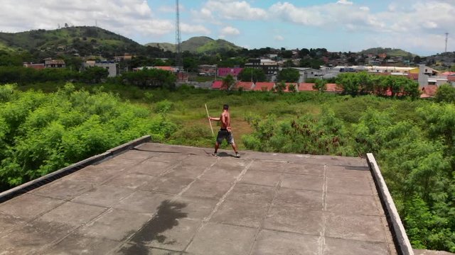 drone video of a man doing martial arts tricks with a pole on a rooftop