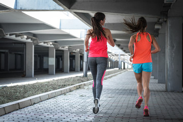 Two female runners jogging around the city road overpass.Urban workout concept.Rear view.