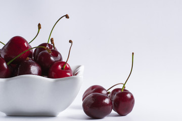 Juicy fruits of a cherry in a ceramic white cup on a white background. Side view. Copy space. Soft focus.
