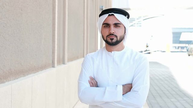 Portrait of Arab man while crossed arms with city background. Arab man looking at the front camera on business location. Daytime shoot of Arabian businessman