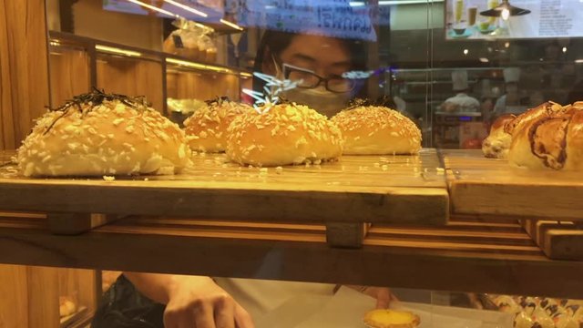 Asian middle-aged woman in a bakery store. Selecting bakery on the shelf.