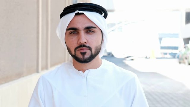 Walking Arab man wearing Kandura on business location. Arabic businessman walks on the city streets wearing dish dasha. Close up of Male Middle Eastern national