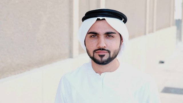 Arab man looks up to the camera smiling. Happy Arabic Emirati national smiles as he looks in front wearing Kandura. Middle Eastern guy on dish dasha UAE menswear