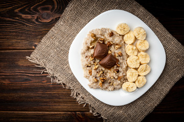 Oatmeal with banana, chocolate and walnut on dark wooden background.