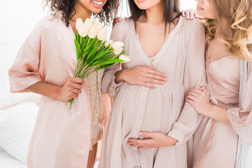 cropped view of young pregnant woman with girlfriends and tulip flowers on baby shower - obrazy, fototapety, plakaty