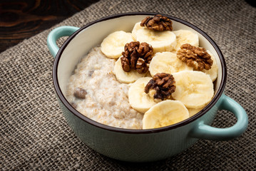 Oatmeal with banana and walnut in green bowl on dark wooden background.