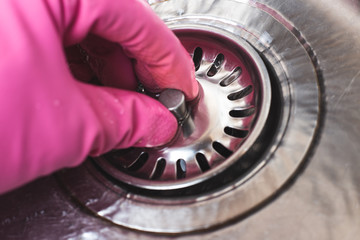 Man in pink glove plugs cork in sink for dishwashing. Save water