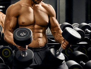 Male bodybuilder holding dumbbells on thighs.