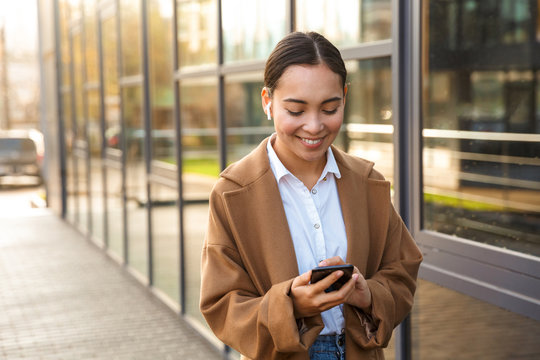 Image of young asian woman using mobile phone and earbuds while walking