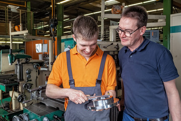 A trainee in the metalworking industry and the instructor check a workpiece using a caliper