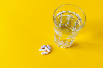 Glass of water and capsule pills on yellow background