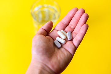 Glass of water and capsule pills on yellow background