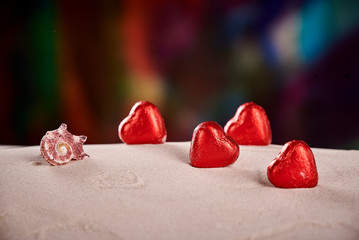 Chocolate red praline hearts on the beach sand on St. Valentine's Day