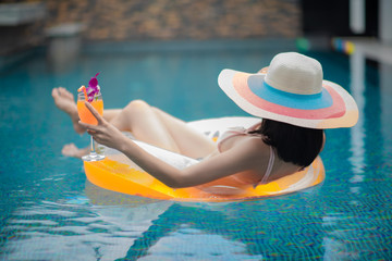 young woman holding orange juice in hand, floatng in inflatable  tube in swimming pool in summertime vacation enjoy