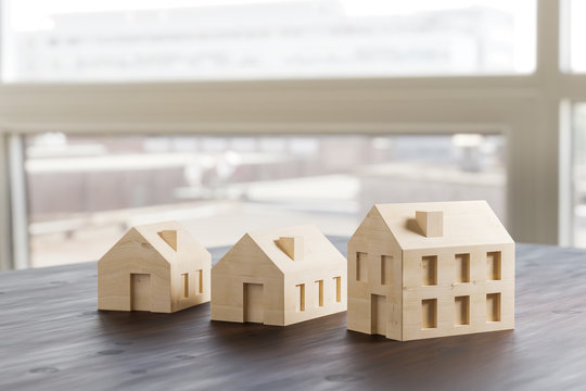Which size of house can you afford? Concept shot: three differently sized wooden models of houses on an architects table