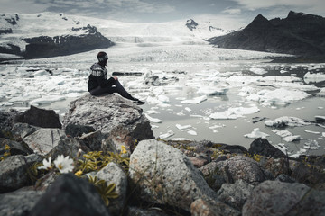 Girl sitting on a stone and watching over fjallsarlon glacier lagoon in iceland. Lagoon is melting due to climate change and you can see a lot of icebergs around. 