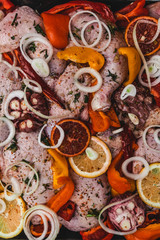raw chicken with onions, garlic and citrus on metal cooking tray, wooden background, top view