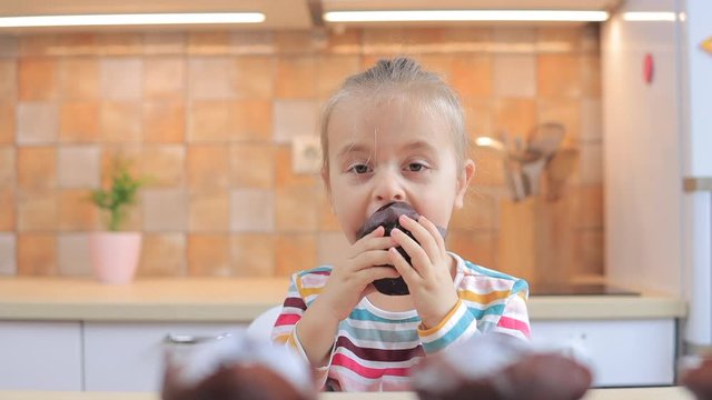 Little girl eating chocolate muffin on the kitchen