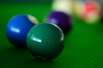 Pool table with pool balls of various colours. Green solid ball is in foreground