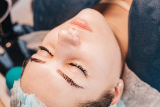 Girl lies with closed eyes during eyelash extension procedure