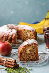 Homemade muffin with apples, bananas and cinnamon, sprinkled with icing sugar on a light blue background, a piece of muffin in the foreground