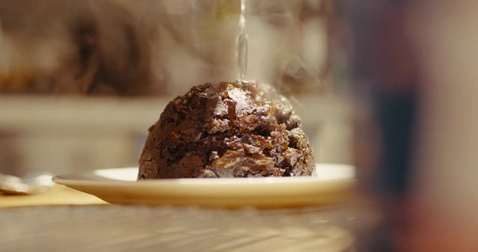Pouring alcohol on Christmas pudding & setting alight, flames burning in dark