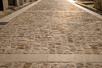 Sidewalk covered with old paving stones in a backlight