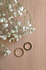 Two gold wedding rings and gypsophila flowers on wooden table. Selective focus.