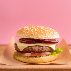 burger on a wooden board on a pink background