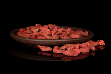 Lot of whole dried red goji berries with brown ceramic coaster isolated on black glass