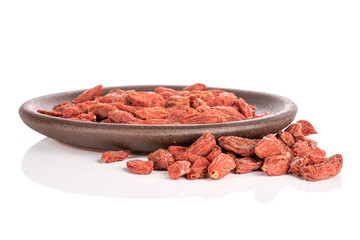 Lot of whole dried red goji berries with brown ceramic coaster isolated on white background