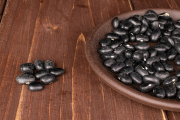 Lot of whole black bean on round bamboo coaster on brown wood